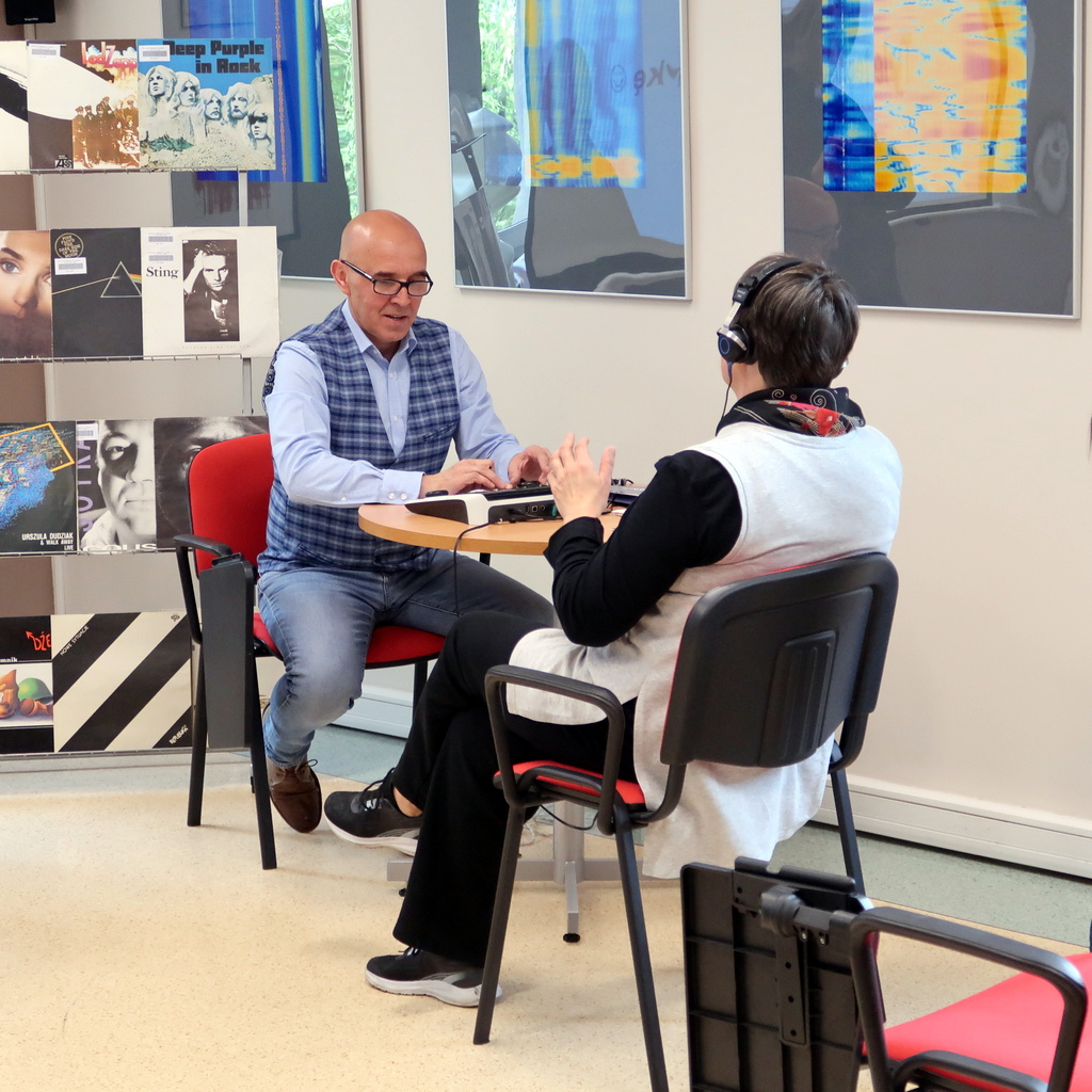 Kobieta ze słuchawkami na uszach siedzi przed mężczyzną sterującym konsolą do badania słuchu