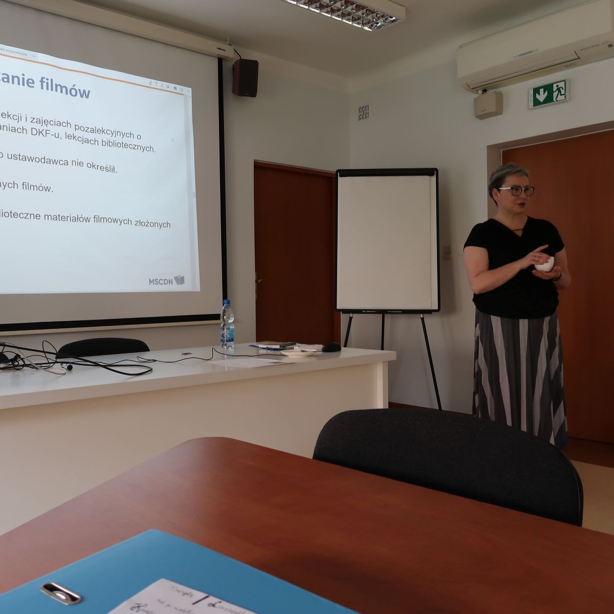Kobieta stoi przed ekranem i wygłasza prezentację w klasie.