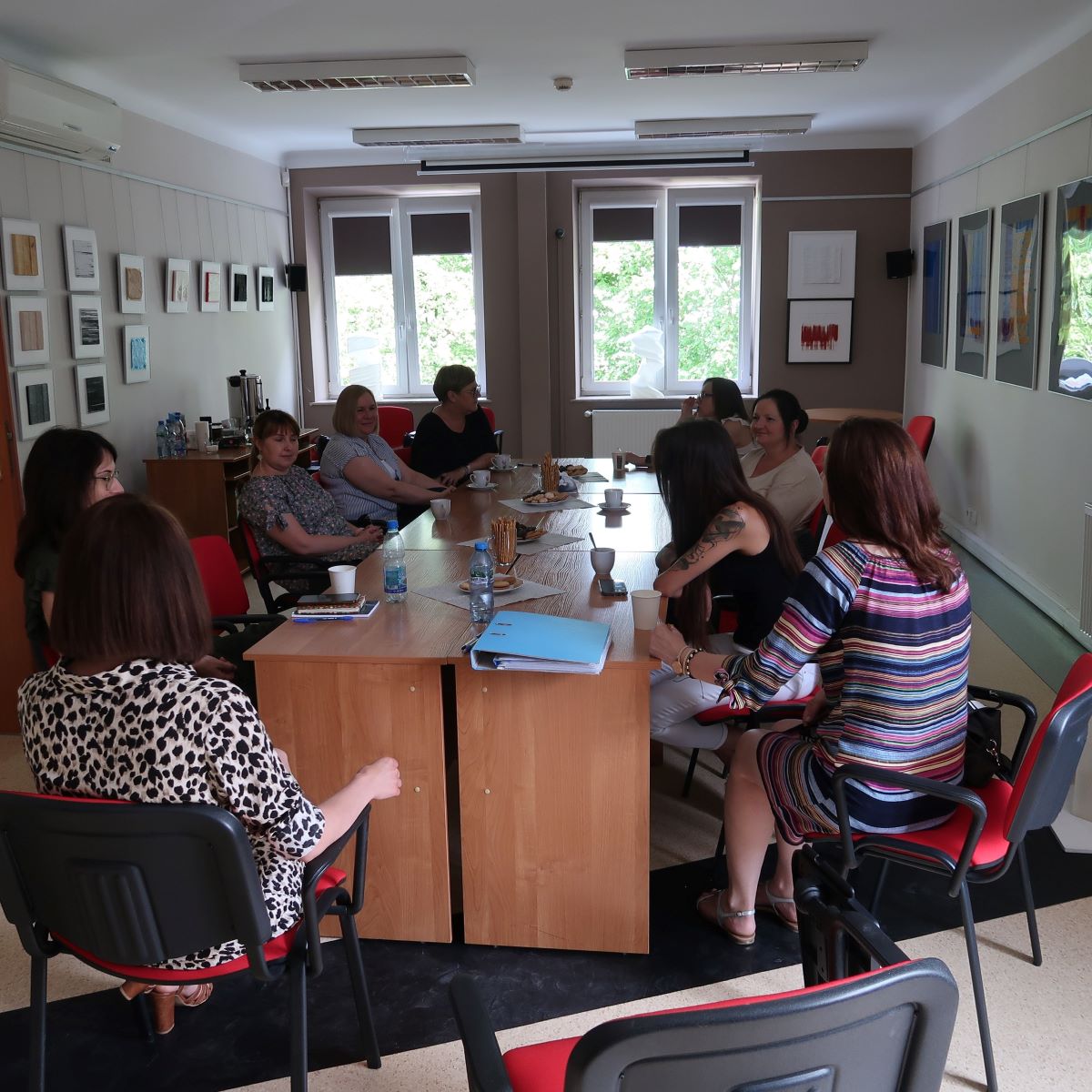 Grupa osób siedzi wokół prostokątnego stołu w dobrze oświetlonej sali konferencyjnej. Są pochłonięci rozmową.