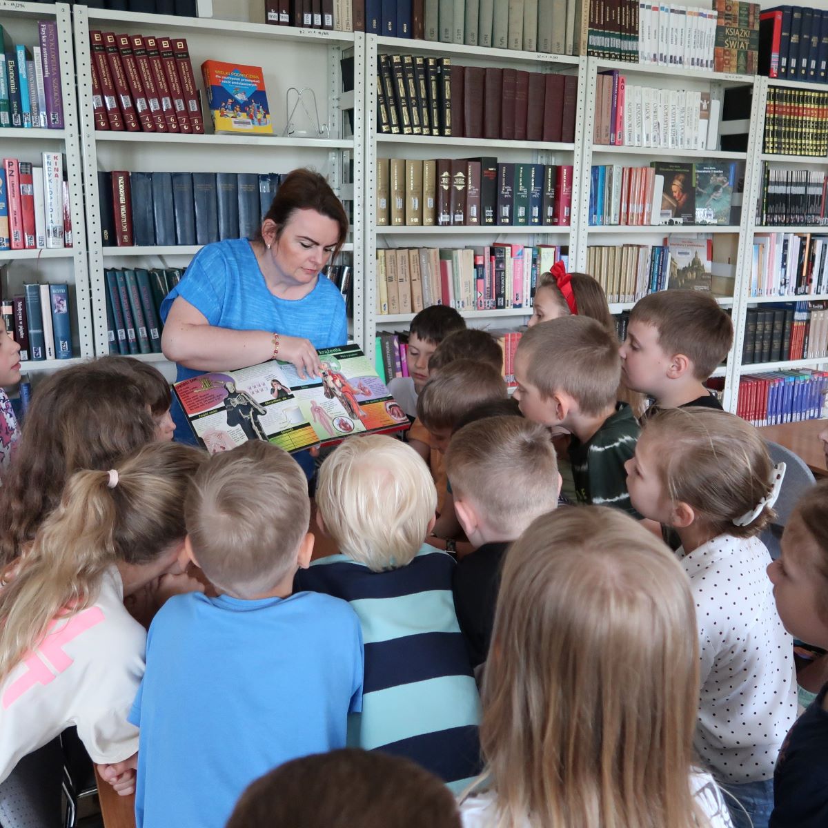 Kobieta pokazuje dzieciom bogato ilustrowaną książkę