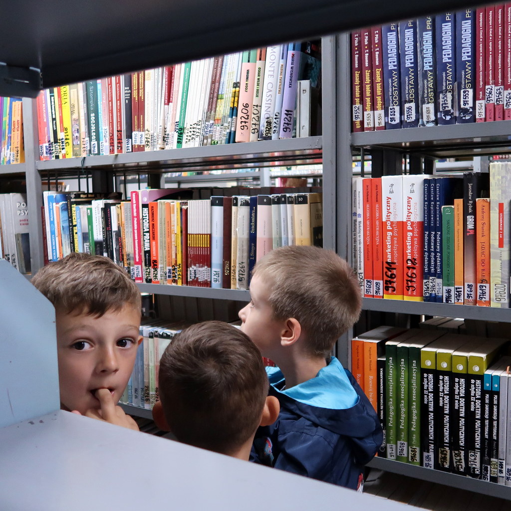 Trzej mali chłopcy stoją miedzy regałami z książkami