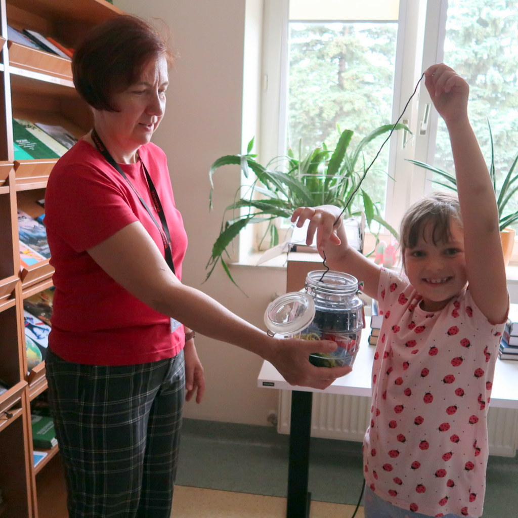 Mała dziewczynka z szerokim uśmiechem wyciąga długą nić ze słoika