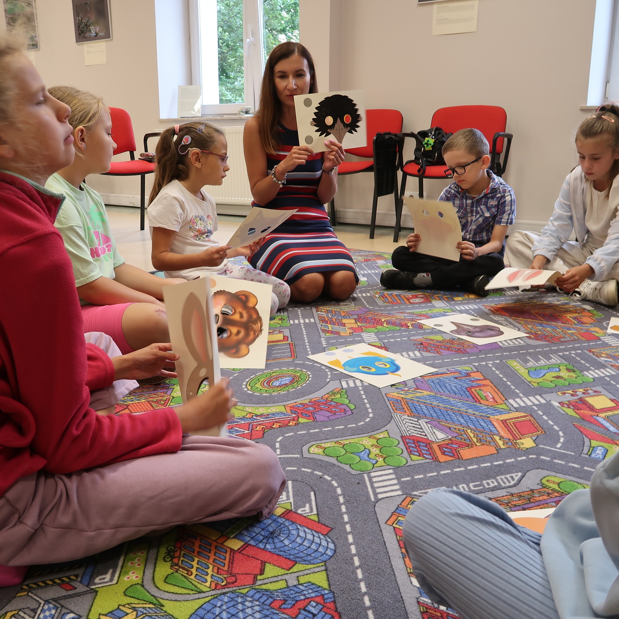 Dzieci siedząc na dywanie ogladają wizerunku zwierząt pokazywanych przez nauczycielkę