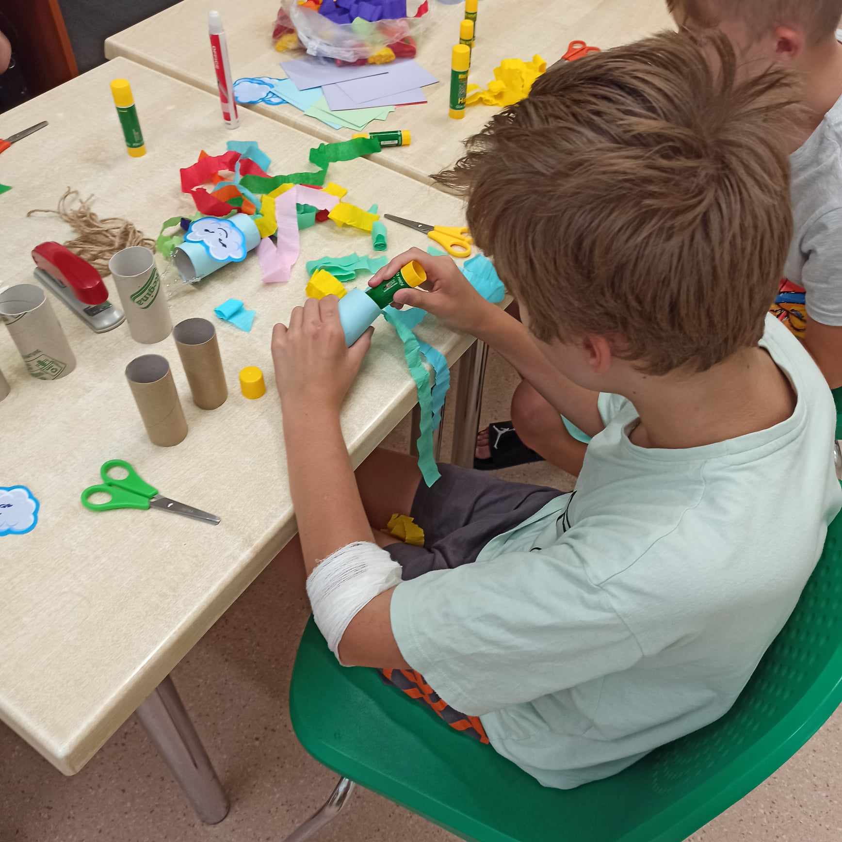 Dzieci siedząc przy stole wykonują prace plastyczne