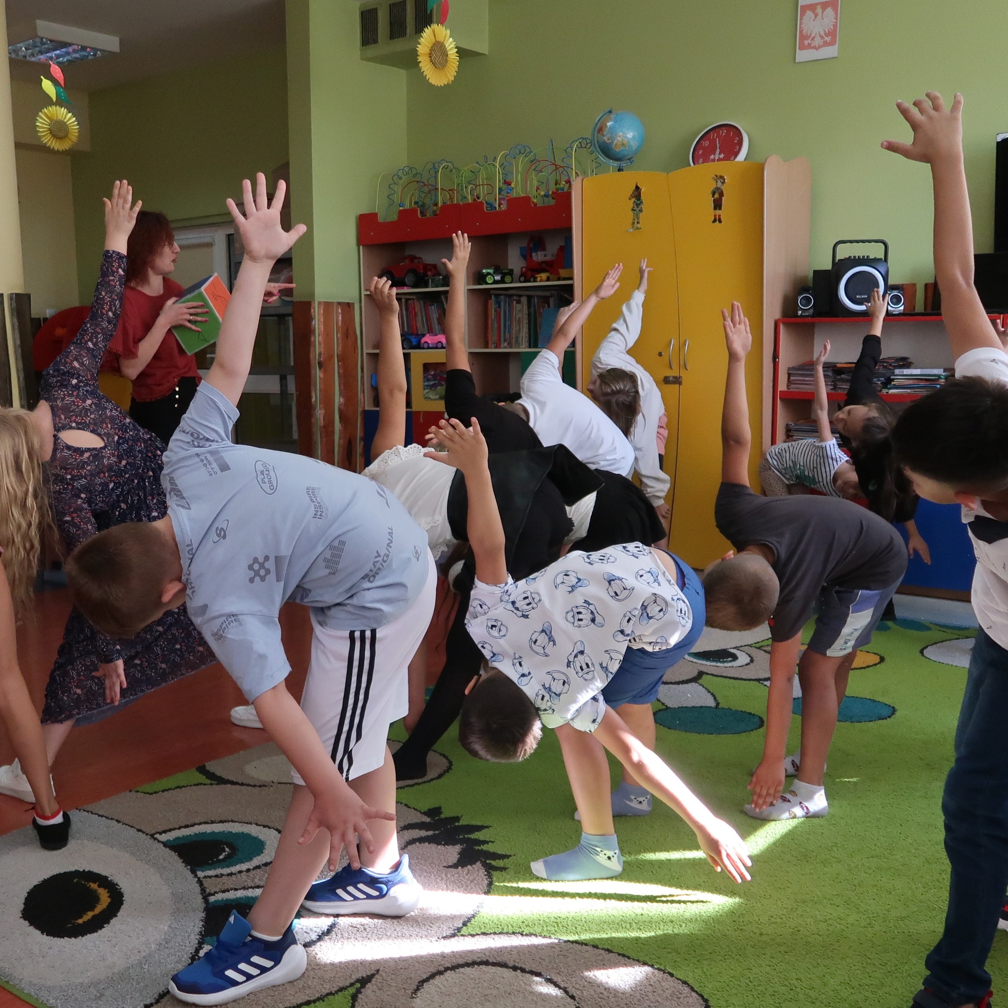 Dzieci wykonują ćwiczenia gimnastyczne pod kierunkiem pani prowadzącej