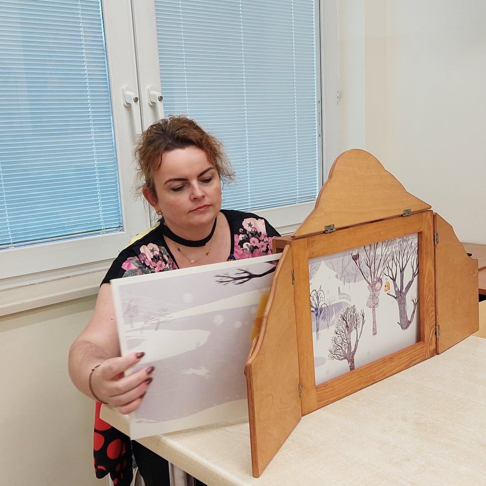 Pani zmienia plansze teatrzyku kamishibai.