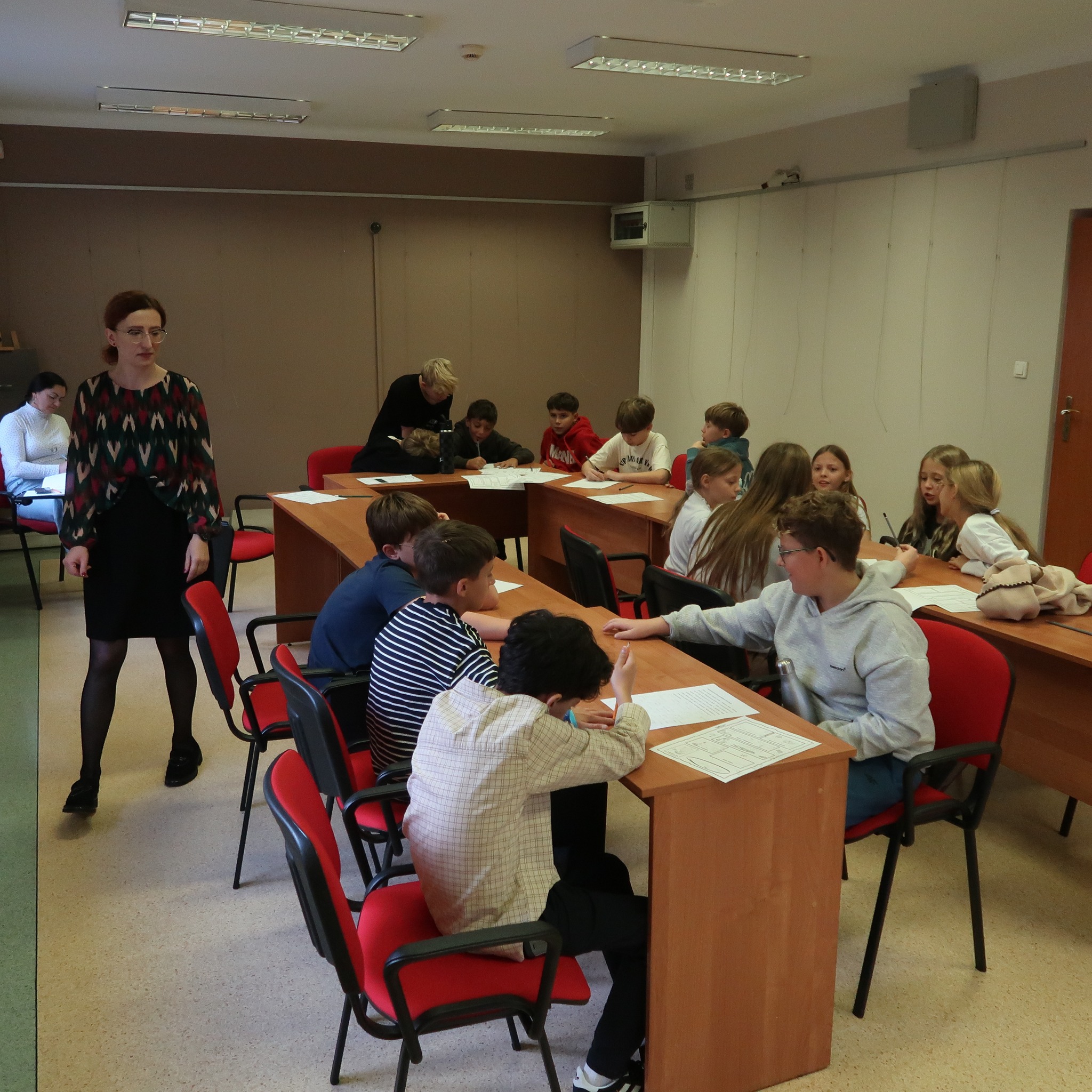 pisarek-2 Dzieci siedząc przy stołach pracują w grupach nad zadaniem