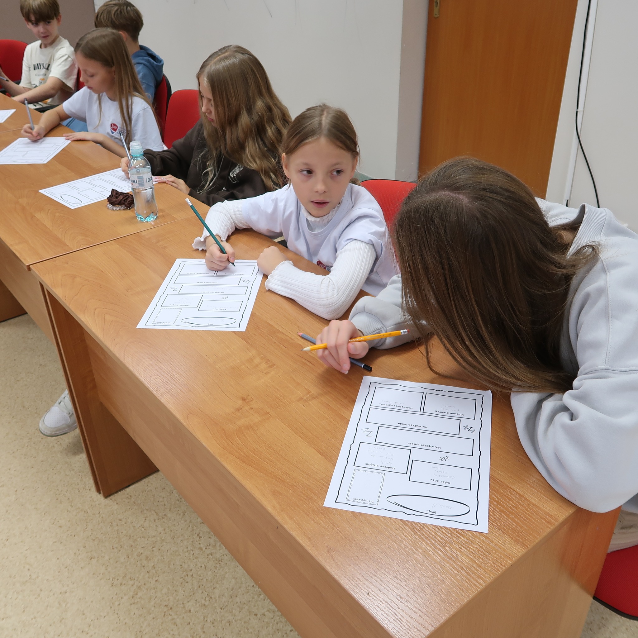 pisarek Dzieci siedząc przy stołach pracują w grupach nad zadaniem