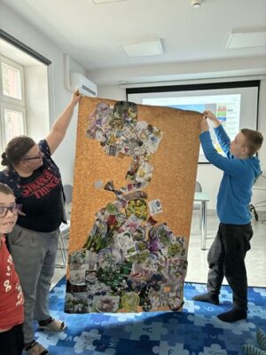 Na zdjęciu widać kobietę i chłopca trzymających duży arkusz papieru z wyklejoną postacią Wiosny.